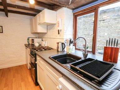 A kitchen with white cabinets a black stove a sink a dish rack knives in a wooden block and a window at Apple Loft in Lostwithiel