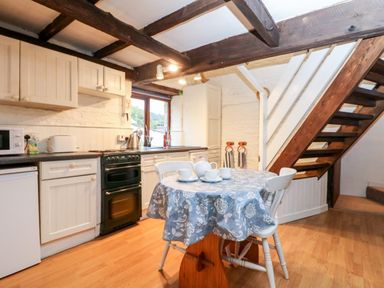 A kitchen with white cabinets a black stove a table with cups and a tea set and wooden stairs at Apple Loft in Lostwithiel