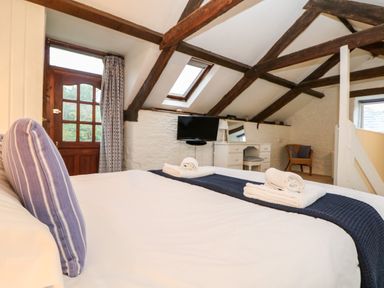 A bedroom with wooden beams a bed with towels and pillows a wooden door a dressing table and a chair at Apple Loft in Lostwithiel