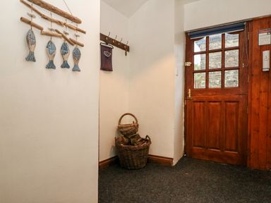 An entryway with a wooden door wicker baskets with firewood on the floor and wooden fish wall decor at Apple Loft in Lostwithiel