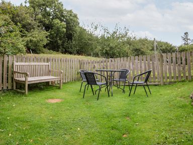 An outdoor garden area with a wooden bench and black metal table with four chairs surrounded by a wooden fence at Apple Loft in Lostwithiel