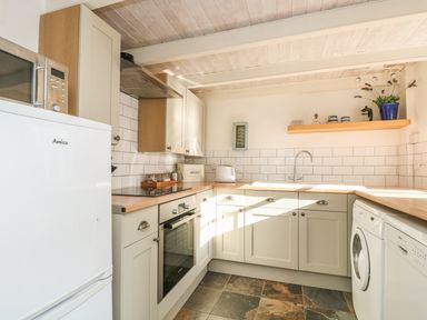 A kitchen with white cabinets wooden countertops a white fridge microwave oven washing machine and dishwasher at Haven in Porthleven