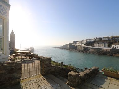A coastal view with a stone patio and metal gate overlooking water and houses on a hillside at Haven in Porthleven