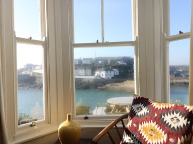 A window view of waterfront houses a round outdoor table and a chair with a patterned cushion at Haven in Porthleven