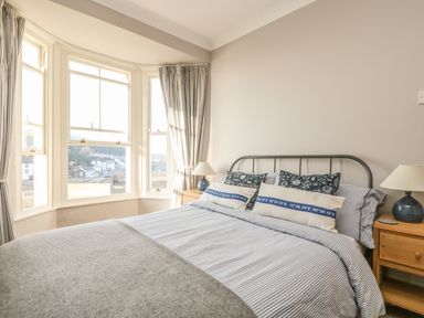 A bedroom with a bed near bay windows and bedside tables with lamps at Haven in Porthleven