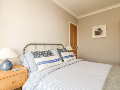 A bedroom with a bed with striped bedding two bedside tables with lamps a wooden door and a framed picture on the wall at Haven in Porthleven