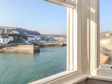 A view of a harbor with stone piers and buildings around the water seen through a window frame at Haven in Porthleven