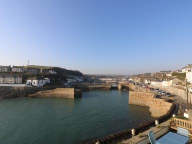 A coastal harbor with stone piers houses along the shoreline and outdoor seating at Haven in Porthleven