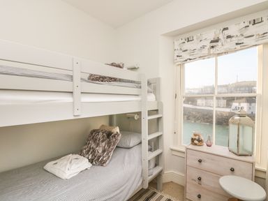A bedroom with a bunk bed a chest of drawers and a window overlooking water at Haven in Porthleven
