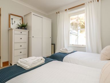 A bedroom with two single beds with towels on top a white chest of drawers with a plant and mirror and a white wardrobe at Haven in Porthleven