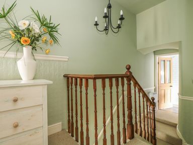 A staircase with wooden railing and a white dresser with a vase of flowers at Haven in Porthleven