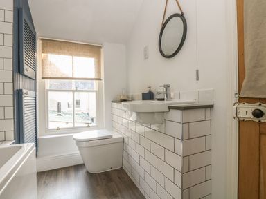 A bathroom with a wall-mounted sink a toilet a window with a blind and a round mirror at Haven in Porthleven