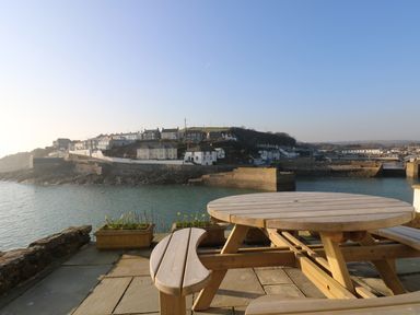 A wooden picnic table on a stone patio overlooking a coastal town with houses and a harbor at Haven in Porthleven