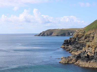 A coastal scene with rocky cliffs and a calm sea at Cockle Island Cottage in Porthallow