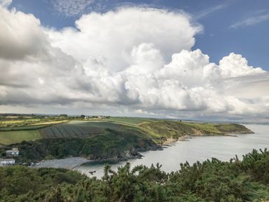 A coastal landscape with cliffs fields and buildings under a cloudy sky at Cockle Island Cottage in Porthallow