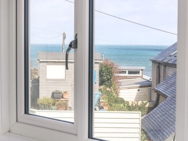A view through a window showing garden sheds plants and the sea at Cockle Island Cottage in Porthallow