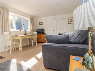A living room with a dining table set for two a gray sofa a wooden cabinet with a television and a side table with a lamp at Cockle Island Cottage in Porthallow