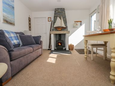A living room with a gray sofa a stone fireplace with a model boat and a wooden dining table at Cockle Island Cottage in Porthallow