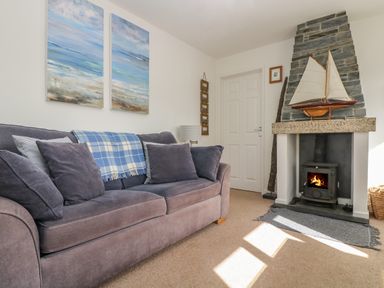 A living room with a sofa a fireplace and paintings on the wall at Cockle Island Cottage in Porthallow