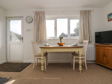 A dining area with a table set for two between a door and a window at Cockle Island Cottage in Porthallow