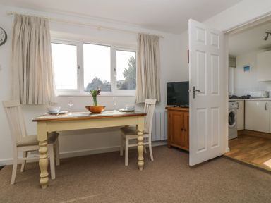 A dining area with a table set for two and a cabinet with a television next to a doorway leading to a kitchen at Cockle Island Cottage in Porthallow