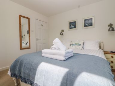 A bedroom with a double bed covered by a blue blanket and white towels on top at Cockle Island Cottage in Porthallow