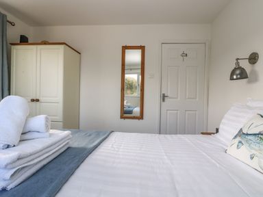 A bedroom with a bed, folded towels, a wardrobe, a wall mirror, and a door at Cockle Island Cottage in Porthallow
