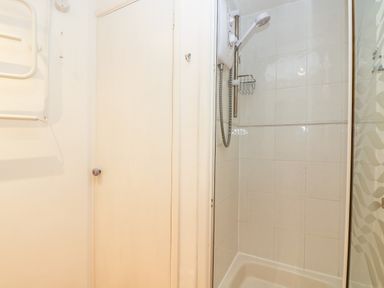 A shower area with white tiled walls and an electric shower unit in a bathroom at Cockle Island Cottage in Porthallow