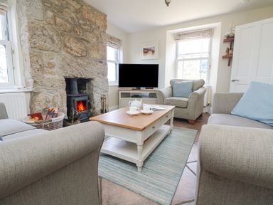 A living room with a stone fireplace a wood stove a coffee table a TV and armchairs at Rose Villa in Newlyn