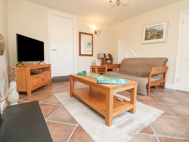 A living room with a wooden coffee table holding a Scrabble game box and a sofa covered with a brown slipcover at Rose Villa in Newlyn