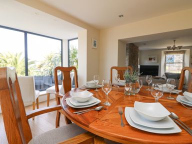 A dining room with a wooden round table set with white plates glasses and cutlery at Rose Villa in Newlyn