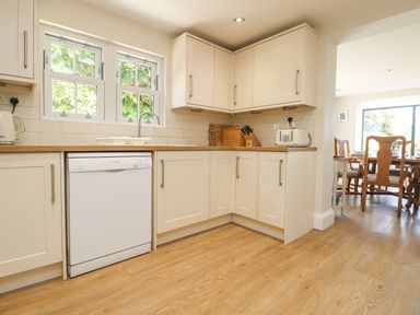 A kitchen with white cabinets wooden countertops a dishwasher and a dining area visible through an open doorway at Rose Villa in Newlyn