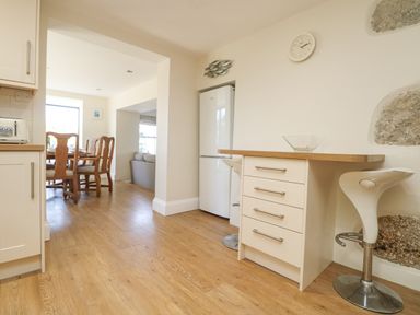 A kitchen area with wooden floor a white refrigerator a wooden dining table with chairs and a white bar stool at Rose Villa in Newlyn
