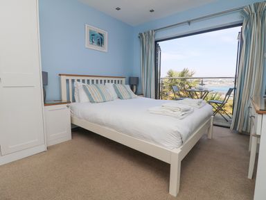 A bedroom with a bed pillows and blankets near an open balcony with chairs and a table at Rose Villa in Newlyn