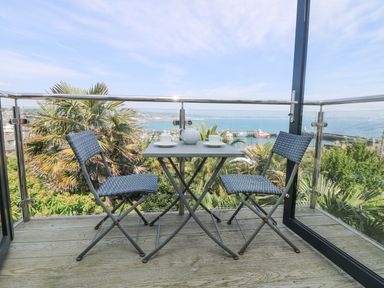 A balcony with a small table and two chairs overlooking a harbor and palm trees at Rose Villa in Newlyn