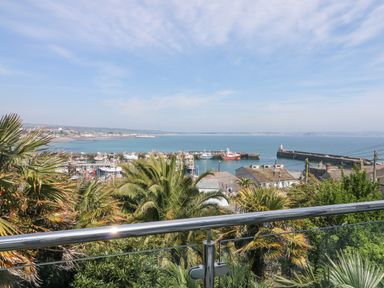 A view of a harbor with boats and a breakwater seen over a balcony with palm trees in the foreground at Rose Villa in Newlyn