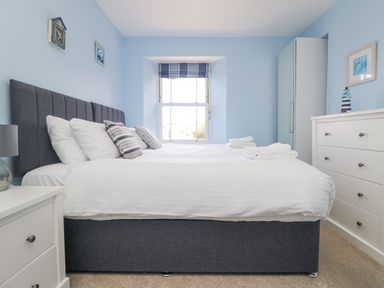A bedroom with a bed pillows and folded towels near a window and dressers at Rose Villa in Newlyn