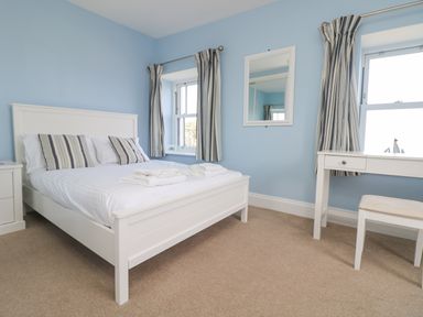 A bedroom with a white bed and striped cushions next to a window with striped curtains and a white dressing table at Rose Villa in Newlyn