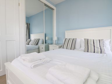 A bedroom with a white bed and striped pillows next to a mirrored wardrobe at Rose Villa in Newlyn
