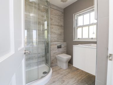 A bathroom with a glass shower enclosure a toilet a sink under a window at Rose Villa in Newlyn
