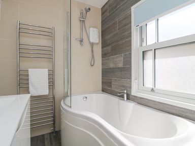 A bathroom with a bathtub shower faucet towel rack and window at Rose Villa in Newlyn