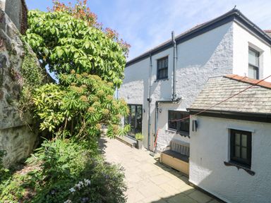 A paved courtyard with plants and trees next to a white two-story building with black-framed windows at Rose Villa in Newlyn