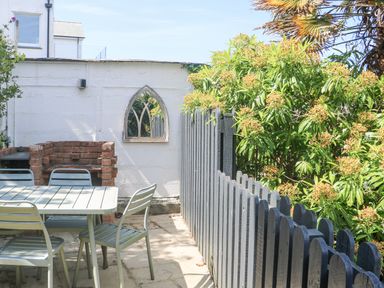 An outdoor patio area with a table and chairs a brick barbecue and a wooden fence at Rose Villa in Newlyn