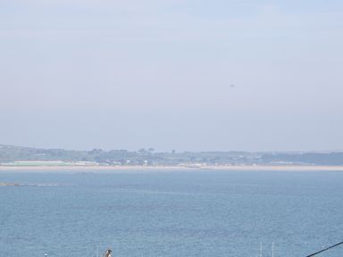 A coastal view with a blue sea in the foreground and a distant shoreline with trees and buildings at Rose Villa in Newlyn