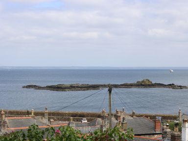 Rooftops and chimneys with a view of a stone pier and rocky island in the sea at Lookout in Mousehole