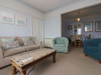 A living room with a sofa armchairs and a wooden coffee table opening to a dining area with a table and chairs at Lookout in Mousehole