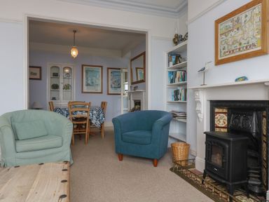 A living room with armchairs and a fireplace next to a dining area with table and chairs at Lookout in Mousehole