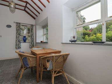 A dining area with a wooden table and four wicker chairs near windows showing greenery at Lookout in Mousehole