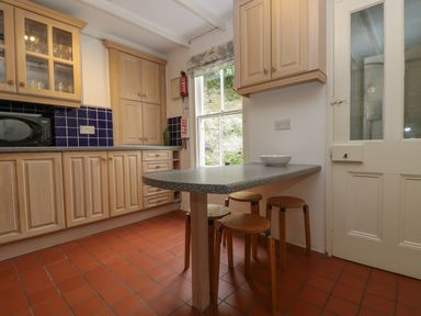 A kitchen with wooden cabinets a microwave a countertop table with stools and a window at Lookout in Mousehole