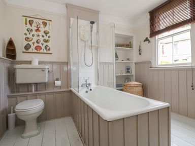 A bathroom with a bathtub shower toilet wicker basket and window blinds at Lookout in Mousehole
